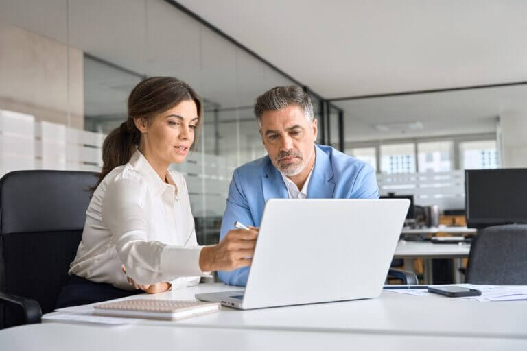 A businessman and woman focused on a laptop while working together in an office environment.