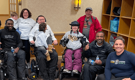 Diverse group of individuals, some in wheelchairs, smiling in a room at a non profit event by CMS.