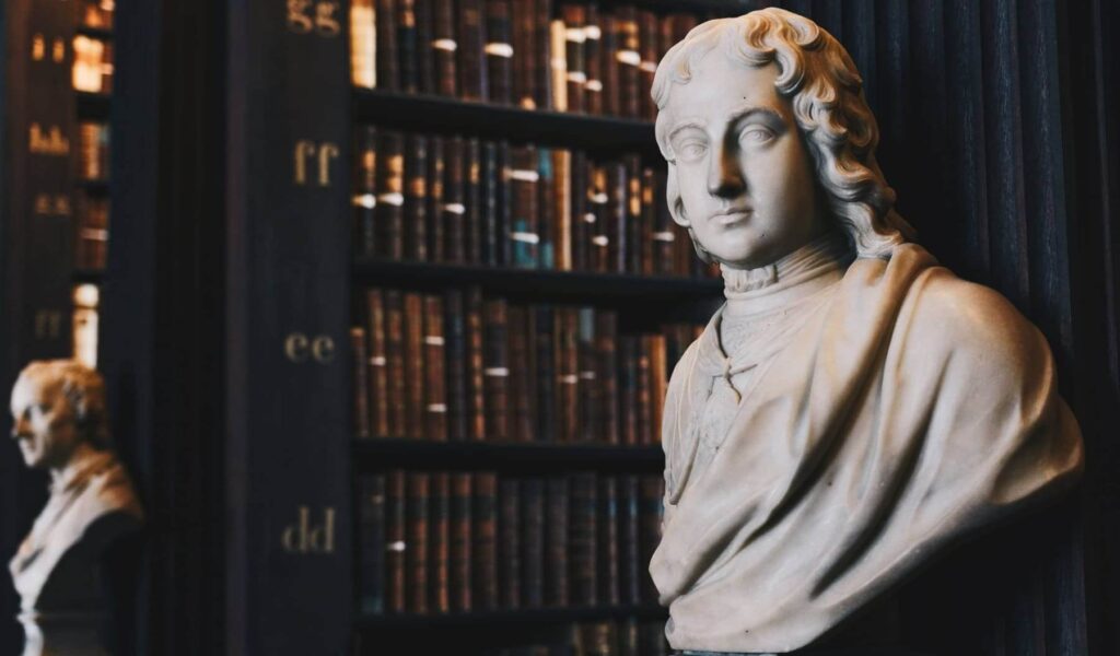 White marble bust of a man in a library with wooden shelves filled with books in the back